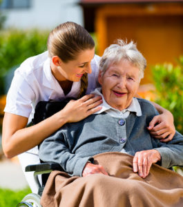 Senior woman in nursing home with nurse in garden sitting in wheelchair